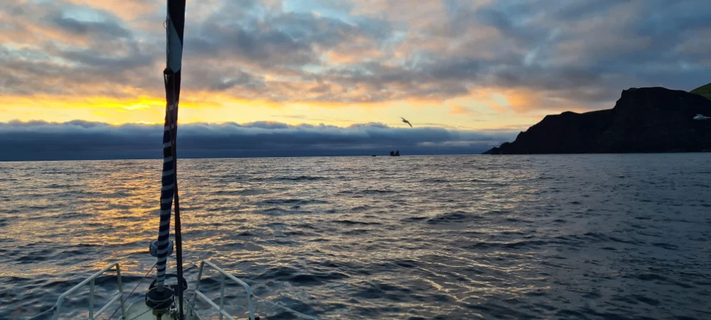Klidná plavba kolem jižního mysu ostrova Jan Mayen se sluncem mezi mraky a přídí naší expediční polární lodě Boomerang.