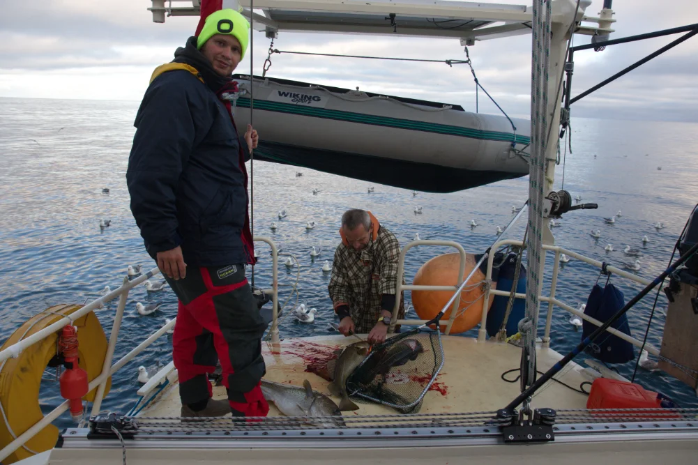Jiří Zindulka kuchá a porcuje ryby na zádi lodě Boomerang pod dohledem syna Kryštofa Zindulky nedaleko ostrova Jan Mayen.