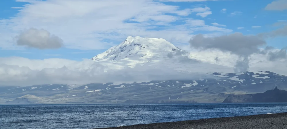 Ostrov Jan Mayen a nejsevernější činná sopka světa Beerenberg pokrytá sněhem, vyčnívající z mraků a tyčící se vzhůru do nebe.